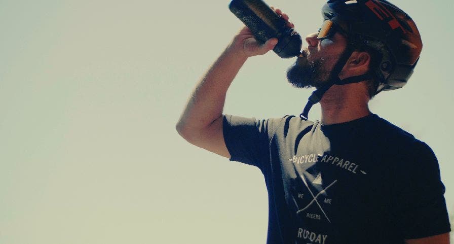 Cycliste homme s'hydratant avec bidon Isostar pendant une course de VTT